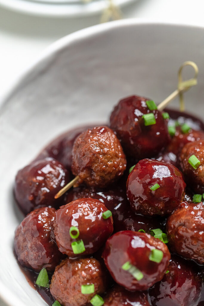 Vegan Grape Jelly Meatballs in a bowl with two on a skewer.
