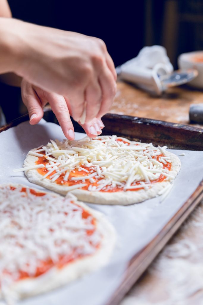 A hand sprinkling vegan cheese on to an uncooked pizza.